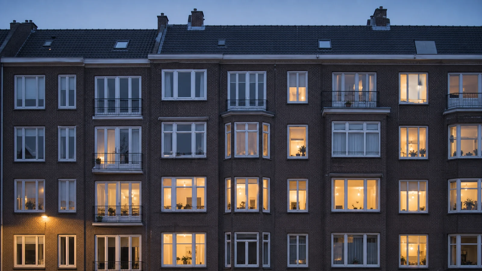 Een Nederlands wooncomplex bij schemer met verlichte ramen.